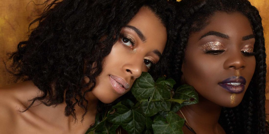 A close up beauty photo of two black young women with ivy and glitter makeup on.