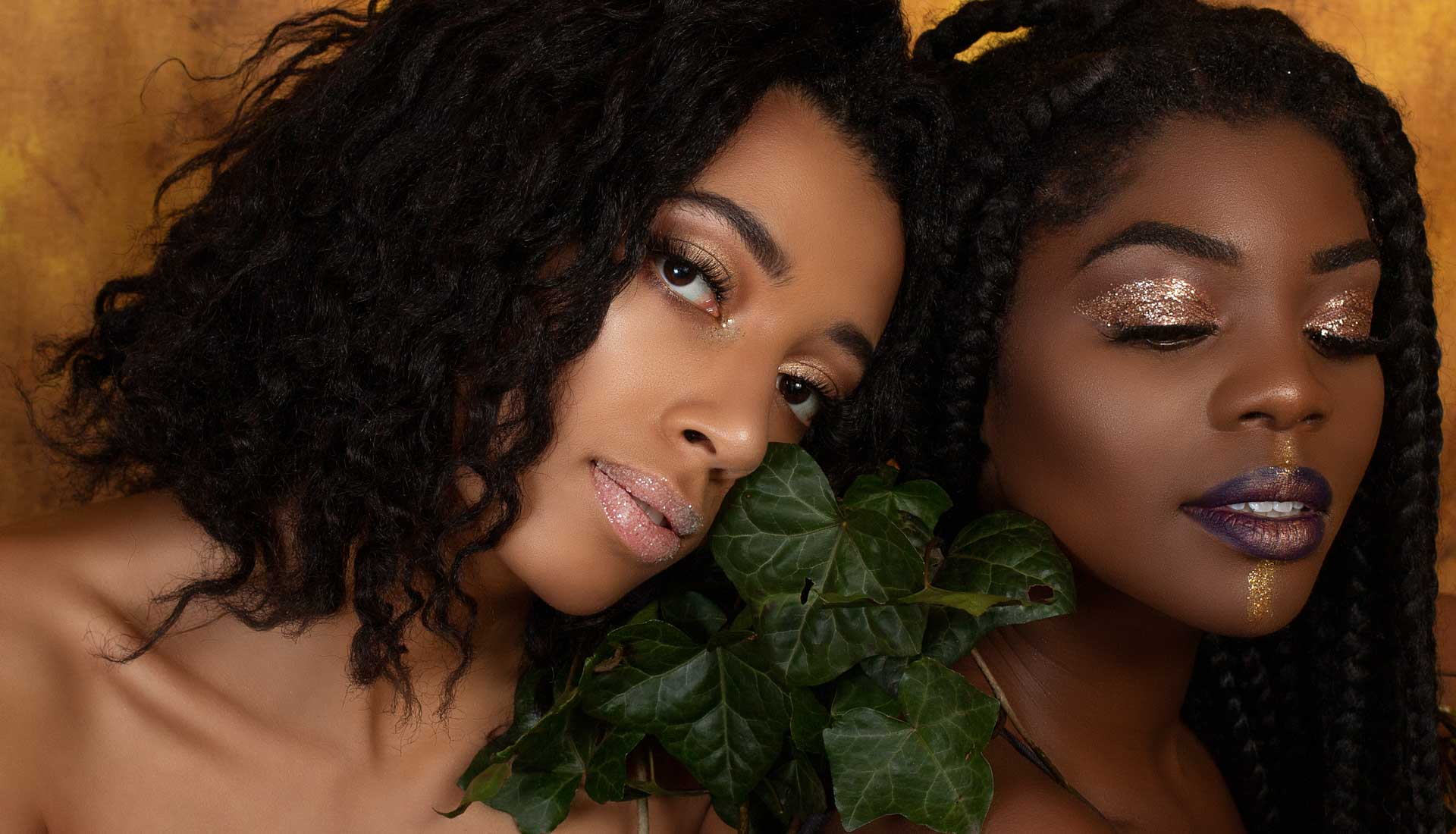 A close up beauty photo of two black young women with ivy and glitter makeup on.