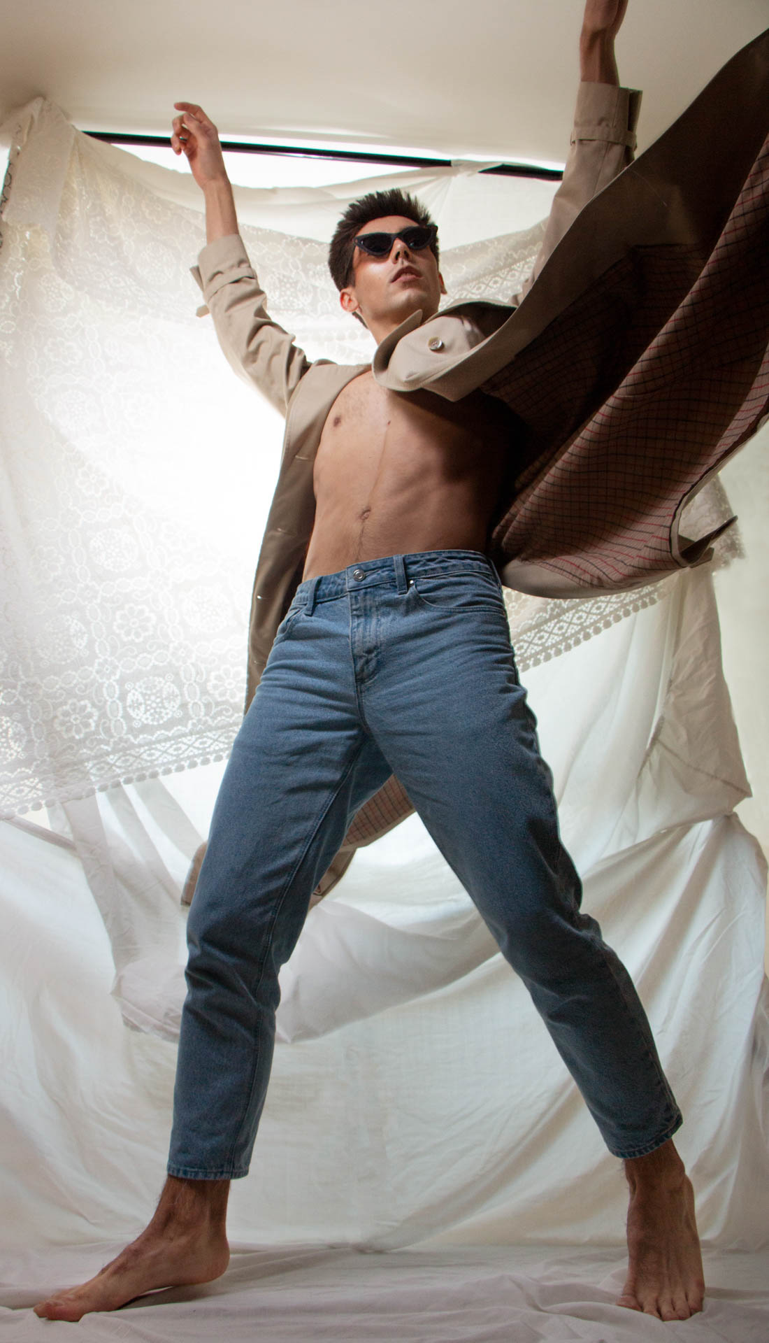 Male dancer is posing with trench coat and blue jeans on in an action pose