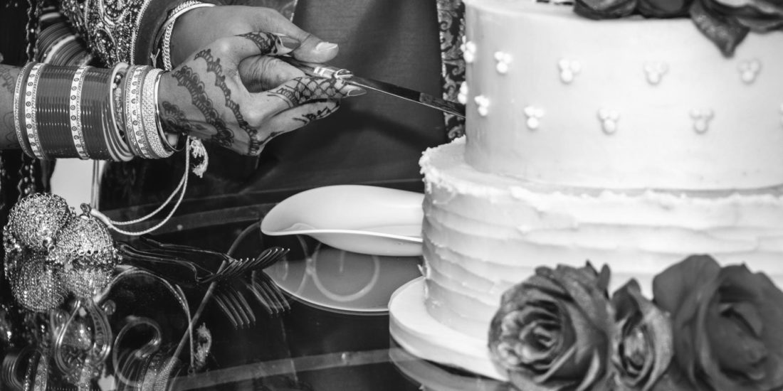 Cutting cake detail photo, Asian bride and groom hands are holding a knife cutting their wedding cake, documentary wedding photographer Birmingham uk