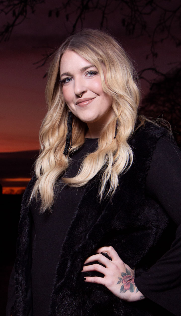 A business headshot of a blond woman wearing all black and posing in front of sunset