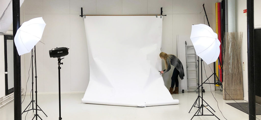 blond woman is setting up white backdrop for a photoshoot