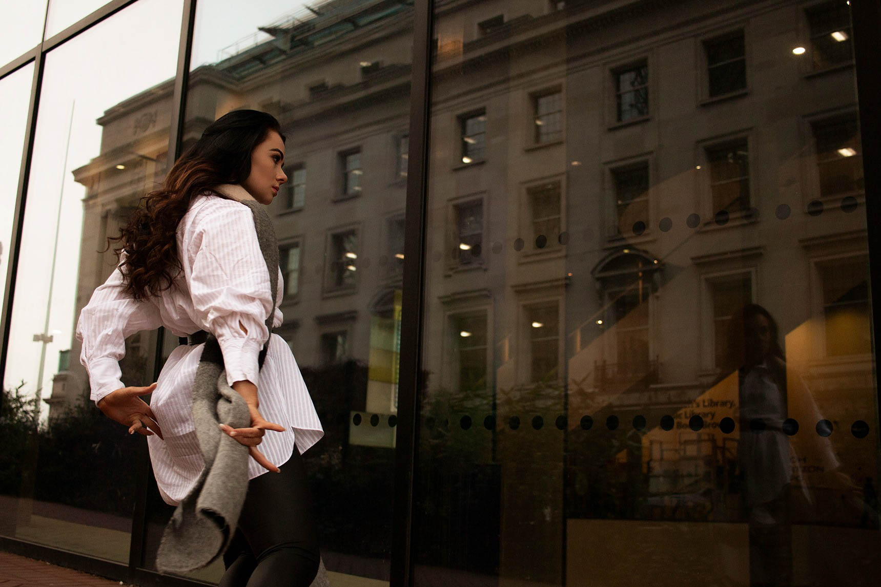 A dark haired dancer wearing white shirt and grey scarf is dancing with her reflection