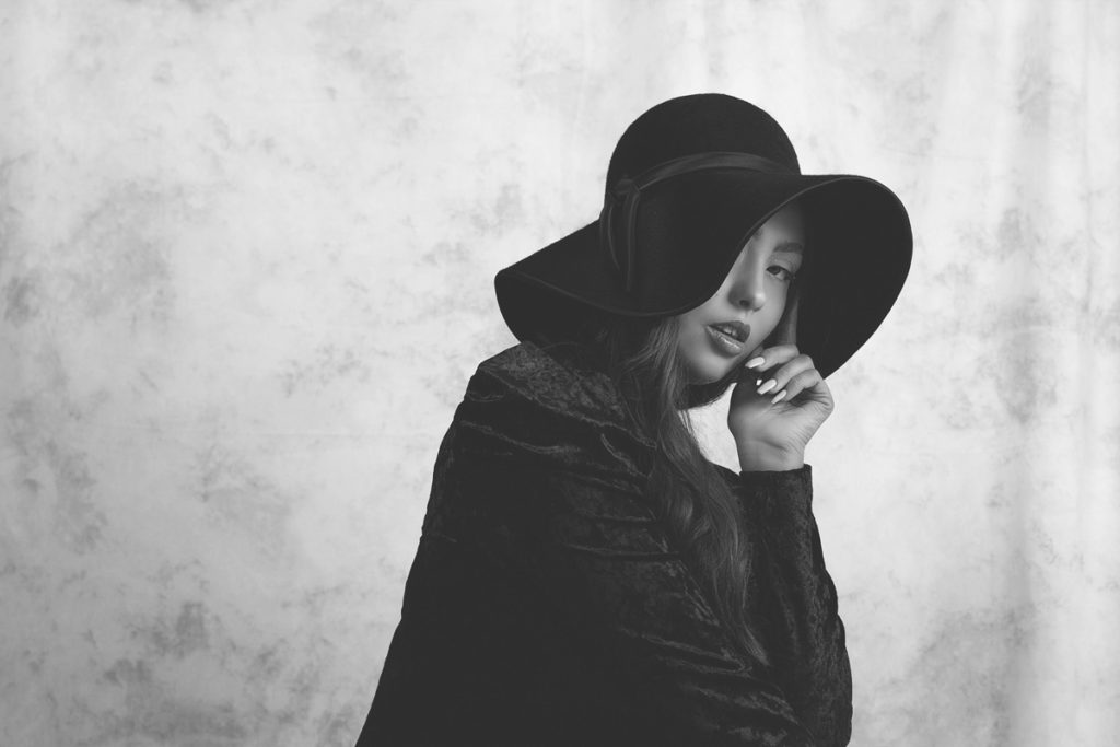 black and white vintage fashion portrait. A young woman wearing black hat and black dress