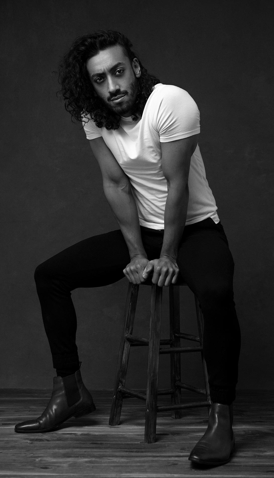 Man with long hair posing on a stool. Editorial portrait photography session