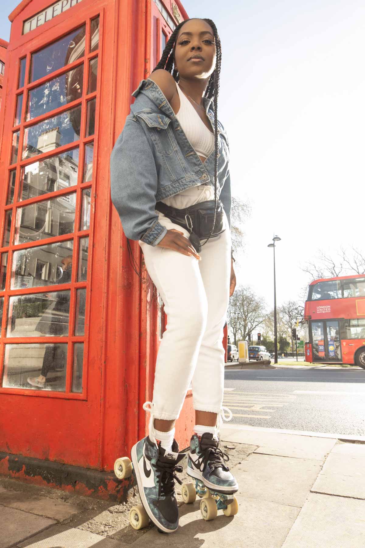 a portrait of a roller skater girl posing by red phone booths in London