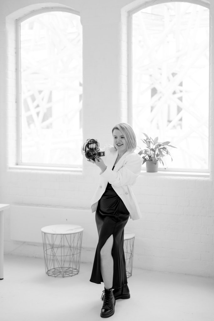 black and white photo of a blond female photographer smiling and taking a photo