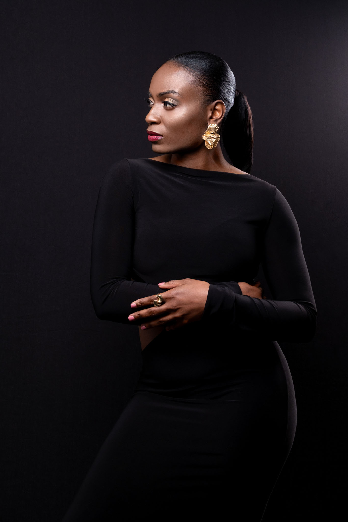 fashion jewellery photography, female model in a black dress on black background wearing large gold earrings a ring