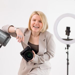 female photographer posing for a photo holding a camera laughing