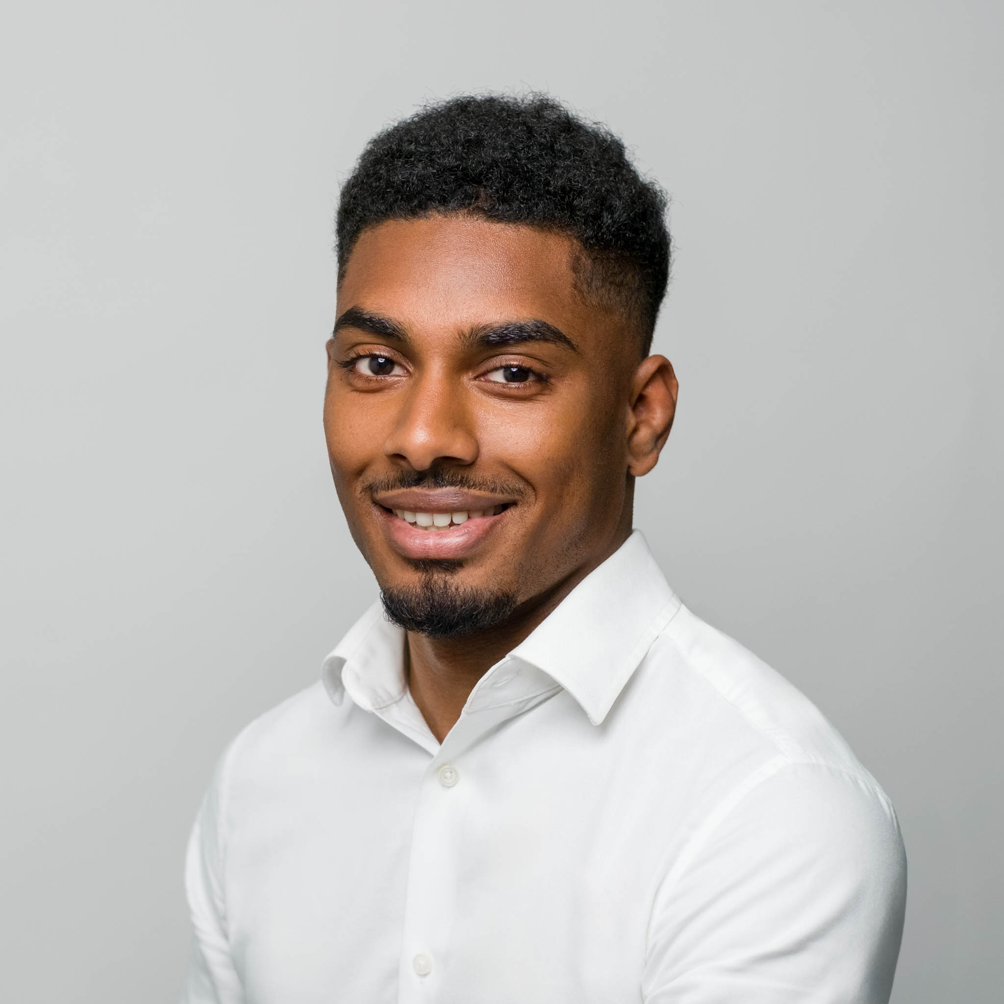 classic professional headshot of a man smiling in front of light grey wall